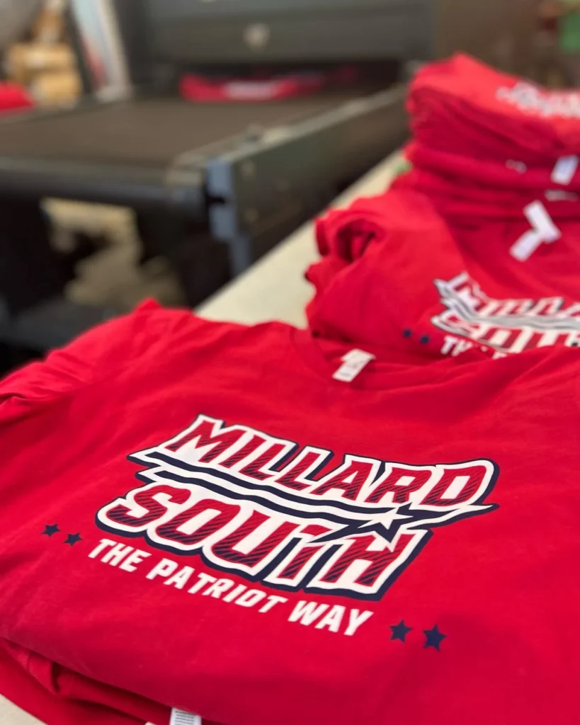 Stack of red Millard South t-shirts with white screen printing